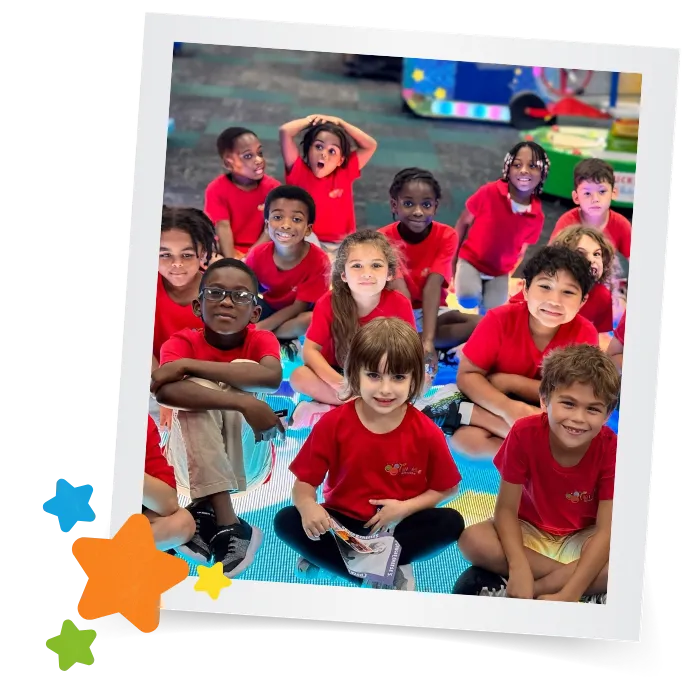 A group of children in matching red shirts sit together on a colorful classroom rug, with star shapes decorating the image at daycare in Houston