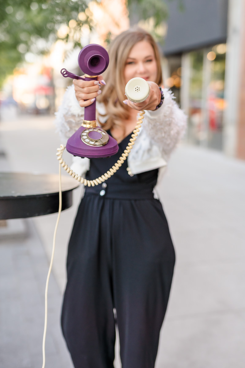 Eva Alexandre, business architecture strategist for experienced consultants, holding a vintage purple telephone toward the camera in an outdoor street portrait.