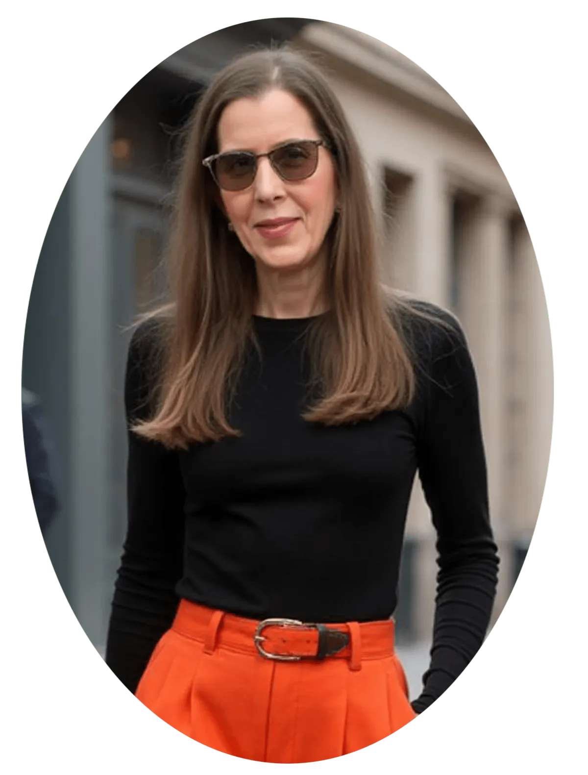 Photograph of Mavery Ellscott walking in street wearing a black turtle neck, orange pants, and sunglasss.