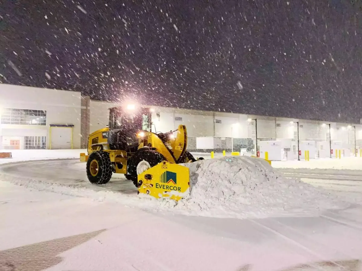 Heavy wheel loaders and industrial plow rigs clearing snow across massive warehouse distribution center loading docks