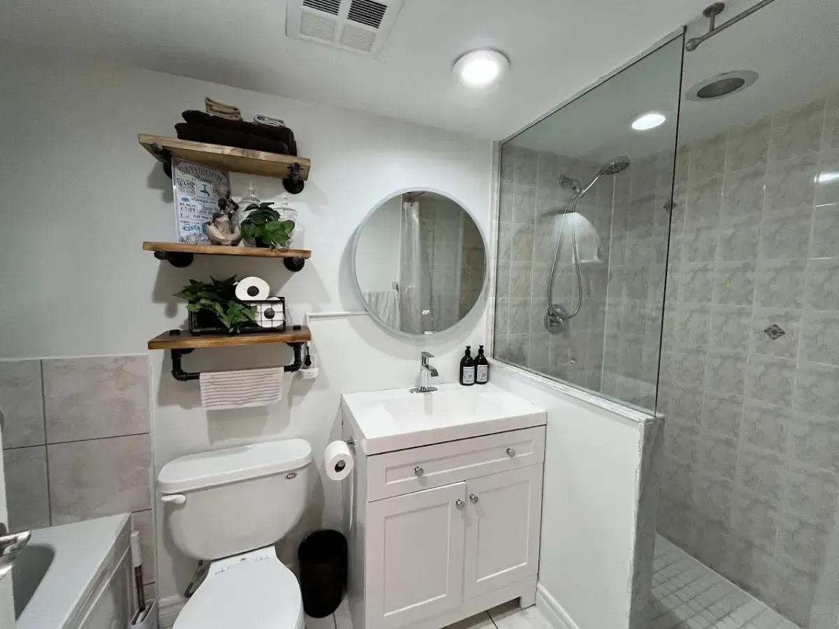Modern spa-like bathroom at Aqua condos featuring a crisp white vanity, round mirror, and glass walk-in shower.