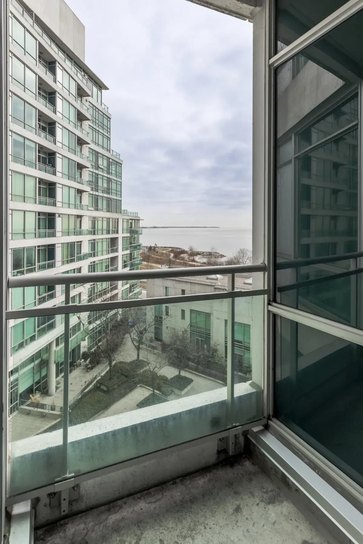Large private balcony at 5 Marine Parade Dr #630, Etobicoke, offering a bird's-eye view of the landscaped courtyard and Lake Ontario.