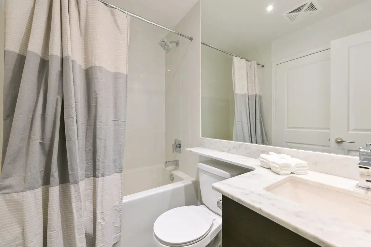 Clean, contemporary bathroom with dark wood vanity and integrated shower/tub at King West Condos.