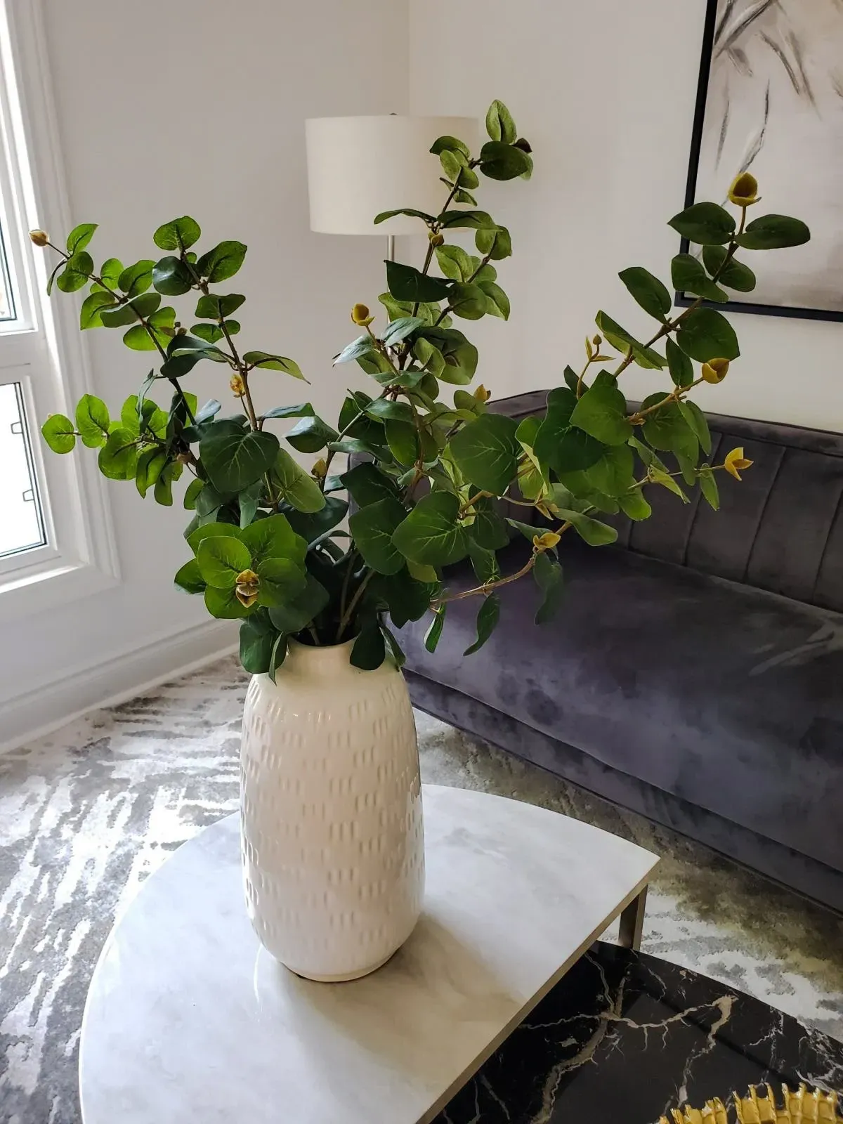 Modern living room corner at 110 Holliday Dr featuring a grey sofa, gold-accented coffee table, and greenery.