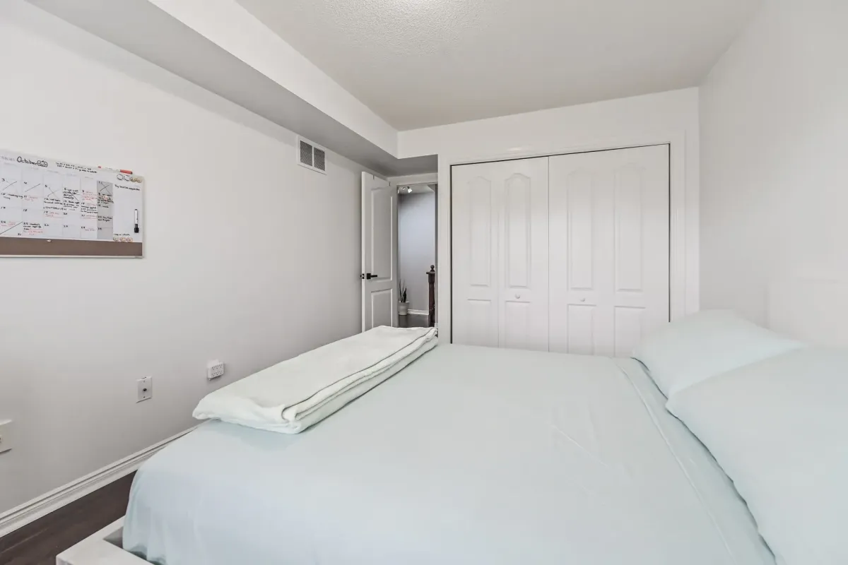 Minimalist bedroom with built-in closets and dark laminate floors at 900 Steeles Ave W #112.