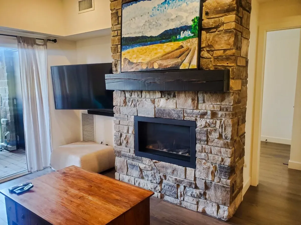 Living area at 11 Beausoleil #105 highlighted by a stunning floor-to-ceiling stone fireplace and timber mantel.