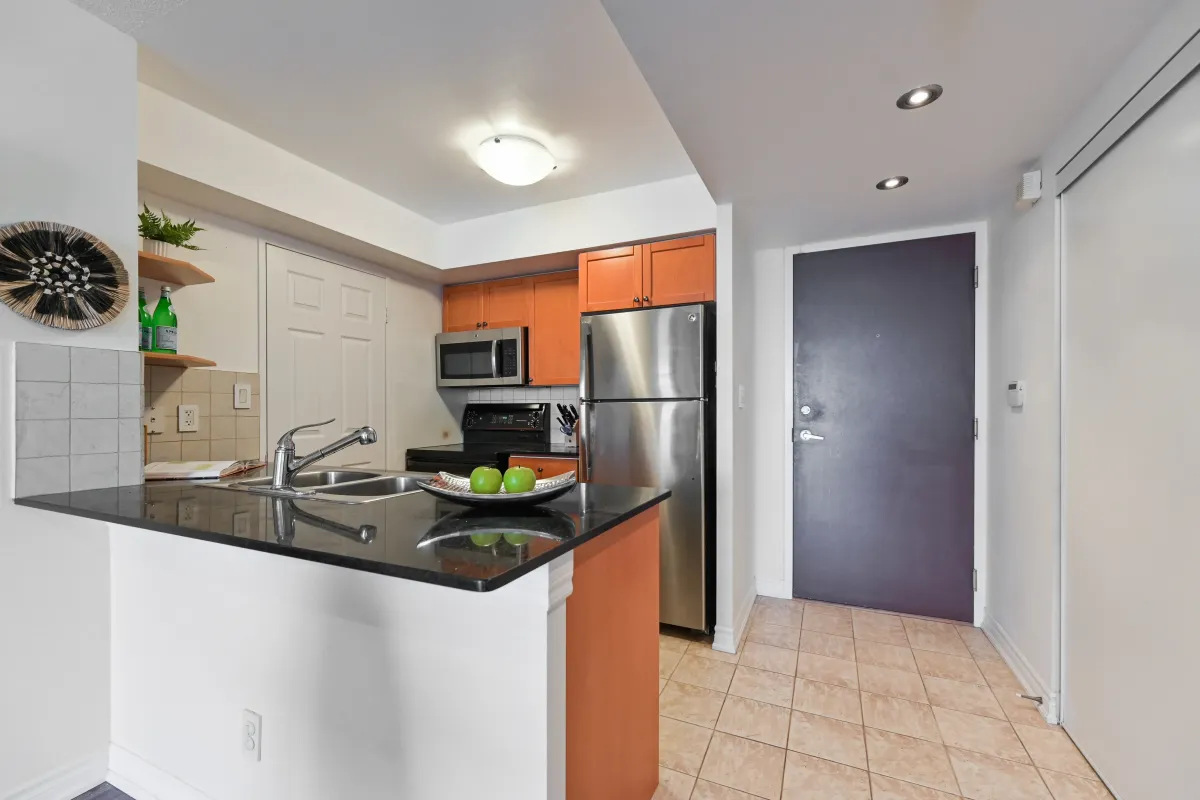Chef’s kitchen in Suite 1416 at 1369 Bloor St W, featuring black granite countertops, stainless steel appliances, and a functional breakfast bar.