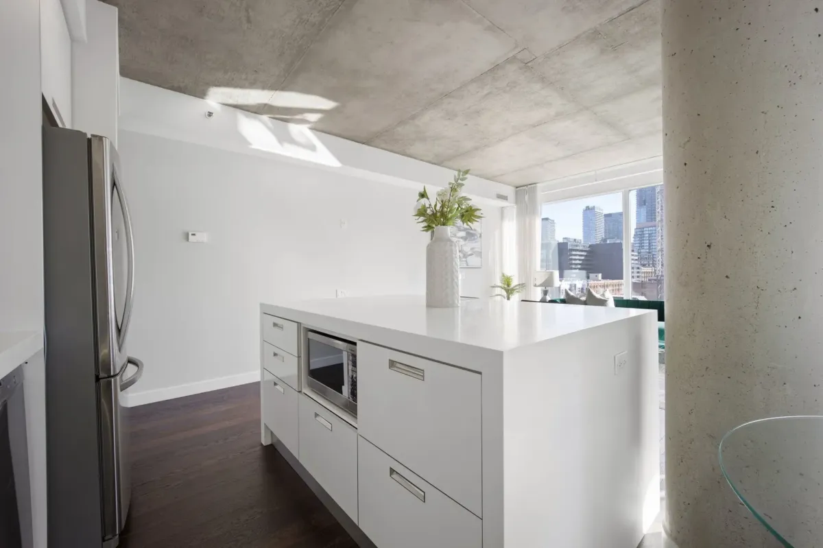 Bright open-concept kitchen at 75 Portland St #807, featuring a large white waterfall island and exposed concrete ceilings.