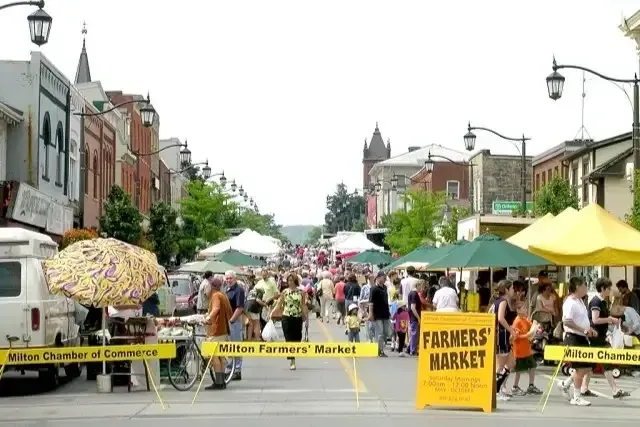 Outdoor stalls and local vendors at the Milton Farmers Market on Main Street during a busy Saturday morning.
