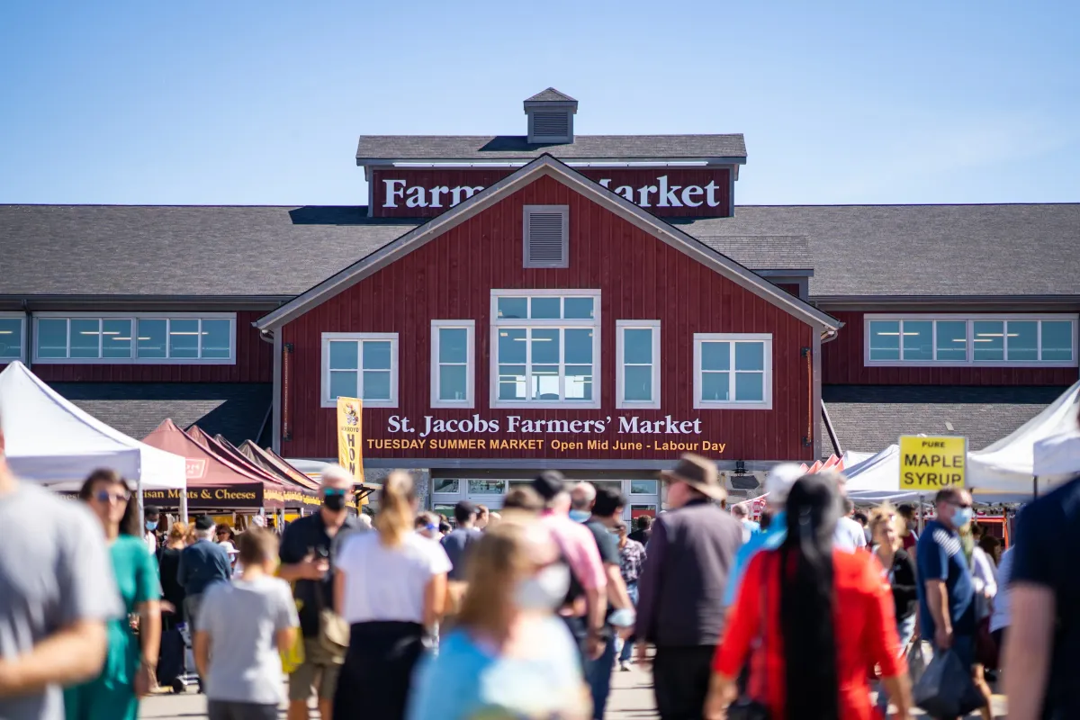 Exterior of the main red building at the St. Jacobs Farmers’ Market with crowds of visitors.