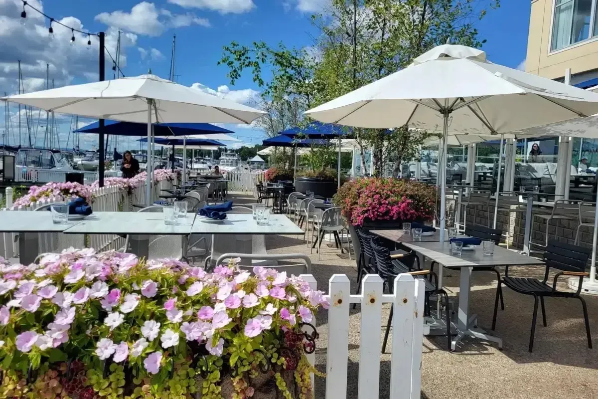 A sunlit outdoor restaurant patio with white umbrellas and flower boxes.