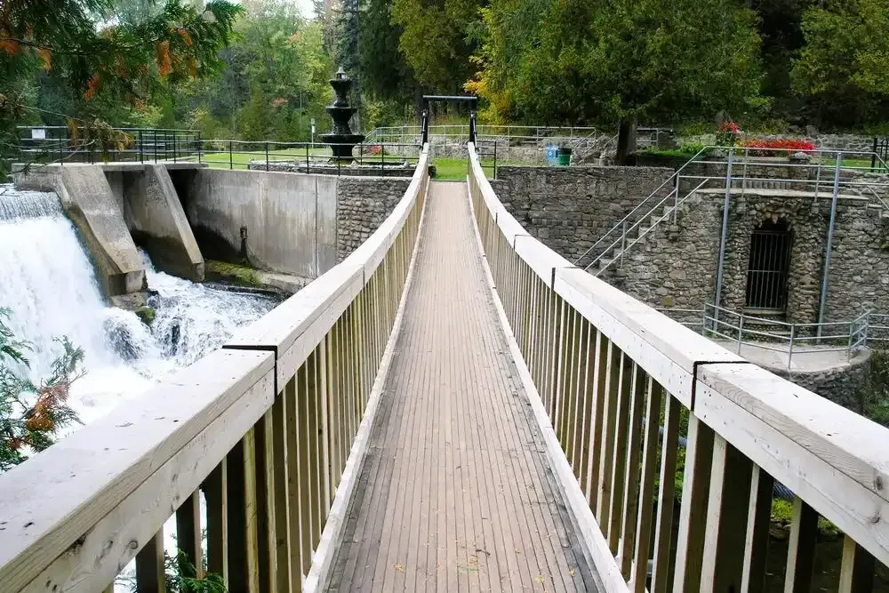 A wooden pedestrian bridge overlooking a waterfall at the Alton Mill Arts Centre in Caledon.
