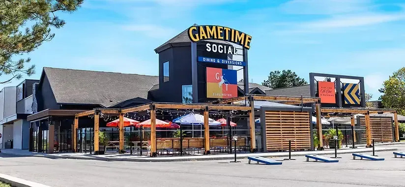 Wide-angle view of the neon-lit arcade floor at GameTime Social Burlington featuring modern redemption games and VR simulators.