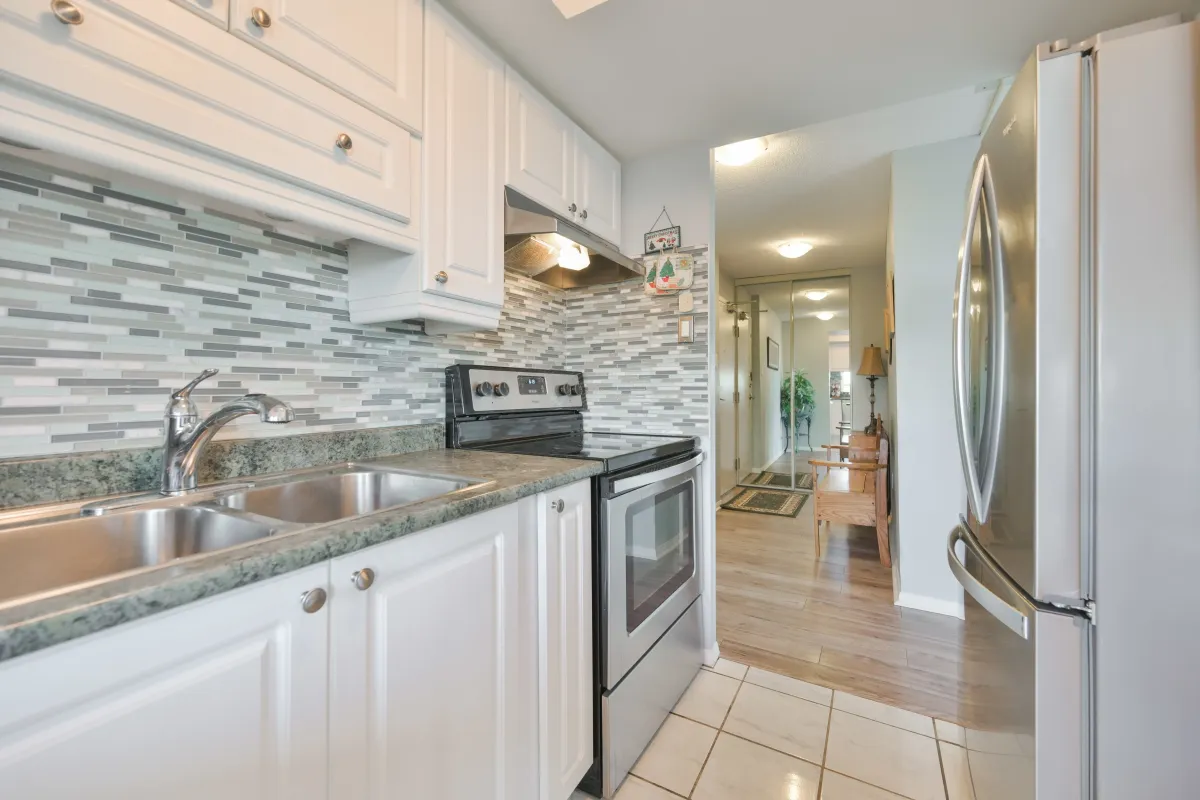 Updated kitchen with white cabinetry, stainless steel appliances, and tile backsplash.