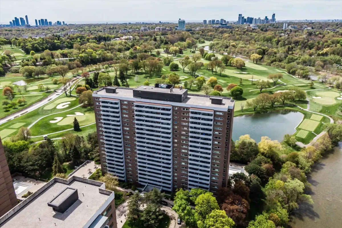 Elevated drone view of the residential brick tower at 240 Scarlett Rd #912 with a golf course and distant city skyline in view.