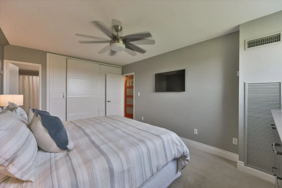 Main bedroom space at 240 Scarlett Rd #912 showing the bed layout, neutral accent wall, mounted television, and ceiling fan.