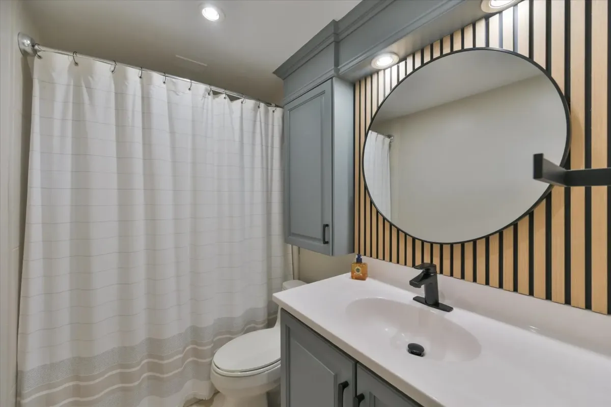 Modern bathroom renovation at 240 Scarlett Rd #912 featuring a white vanity sink, black round mirror, and wood slat accent wall.