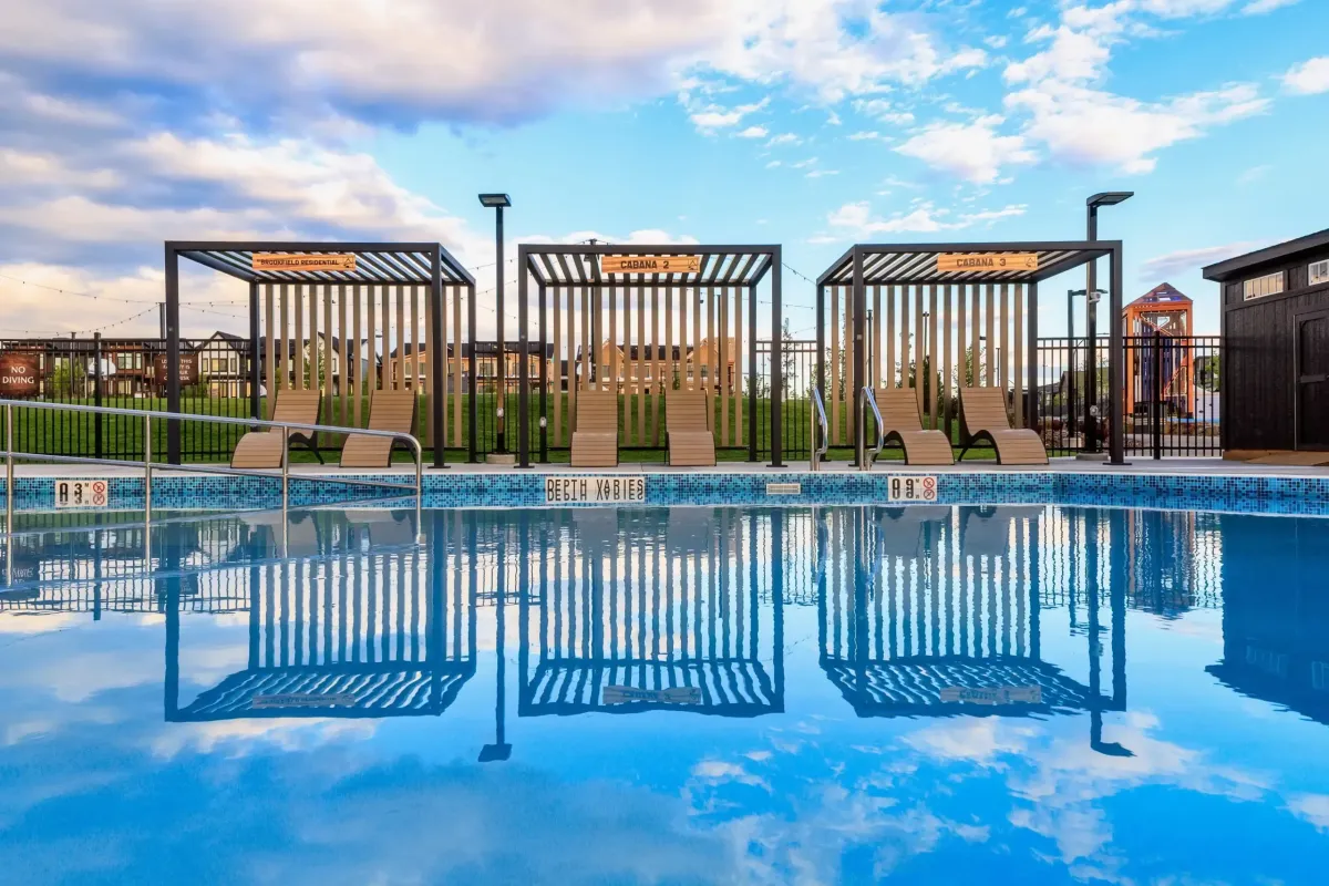 Rockland Park NW Calgary poolside view showing three modern black metal cabanas and lounge chairs reflecting in clear blue water.