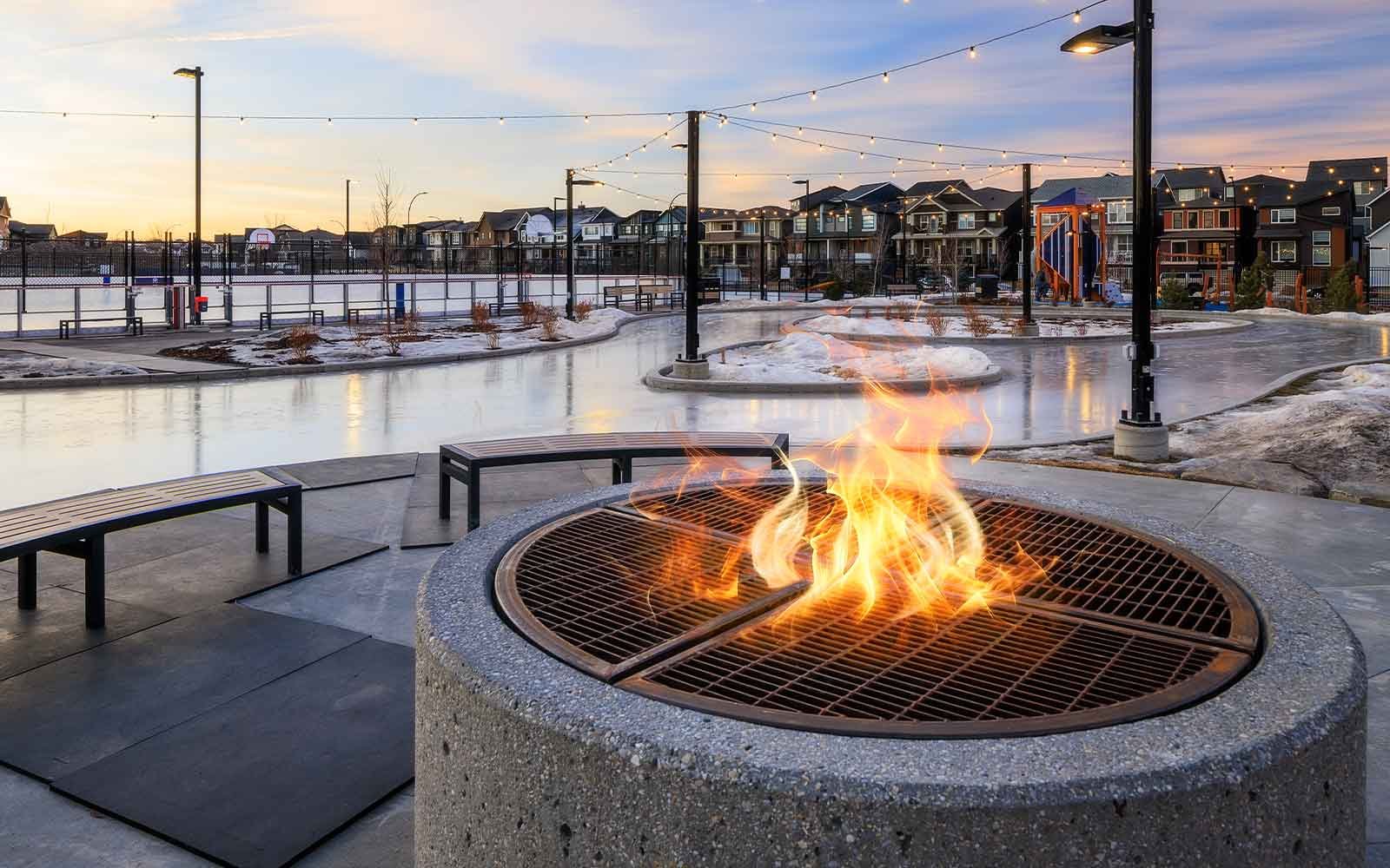 Rockland Park NW Calgary concrete outdoor gas fire pit burning next to a community leisure ice skating trail at dusk.