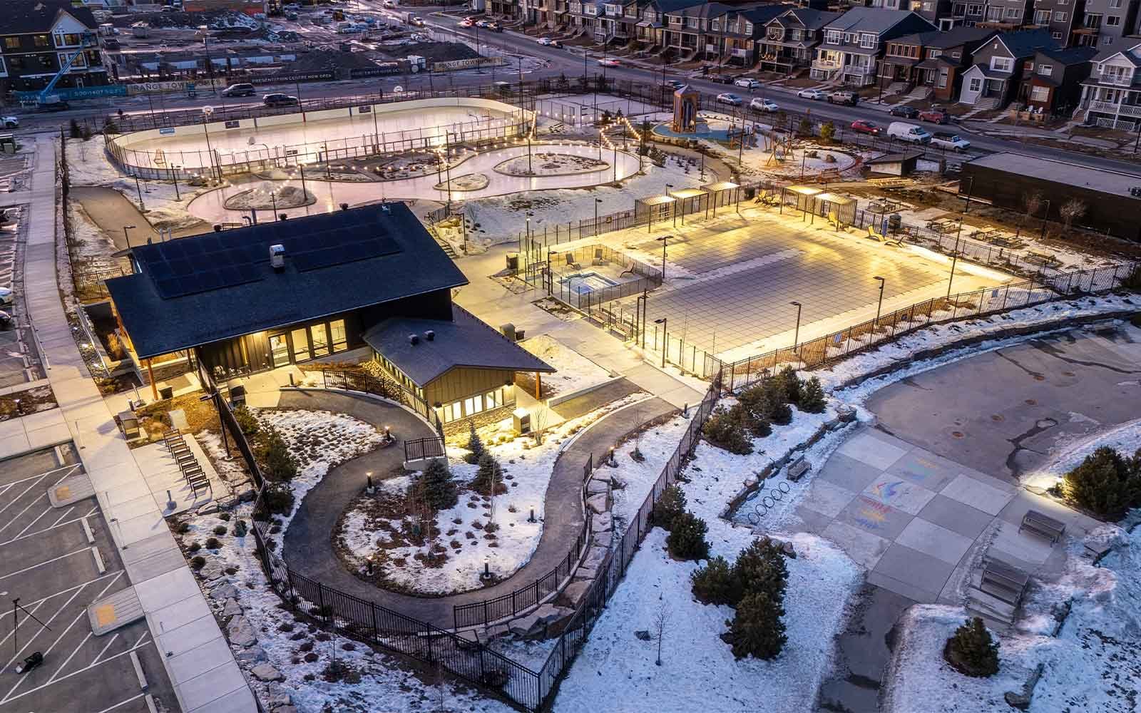 Rockland Park NW Calgary elevated winter aerial view of illuminated community facility pathways, outdoor rinks, and light snow.