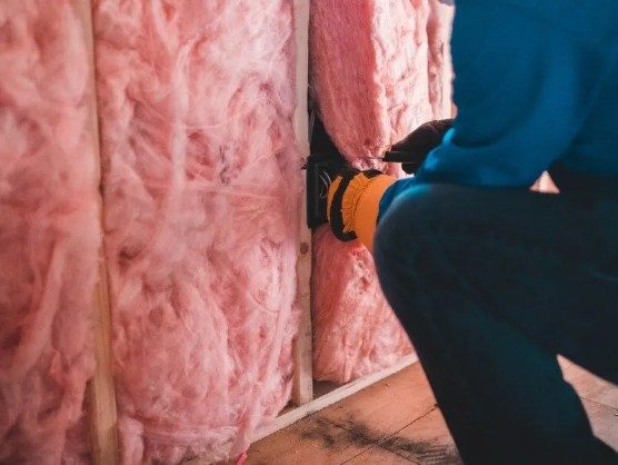 A person is installing pink fiberglass insulation between studs in a wall.