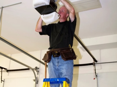 A man on a ladder is installing a garage door opener.