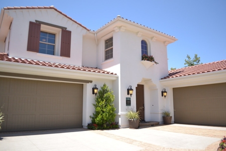 A white stucco house with a red tile roof features a two-car garage on the left and a single-car gar…