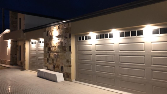 A modern house with two garage doors and stone facade is illuminated at night.