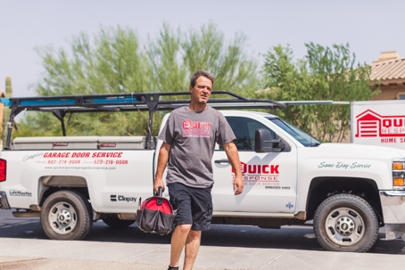 A man holding a toolbox walks in front of a garage door service truck.