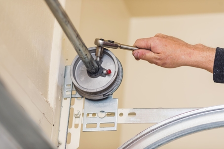 A person is tightening a part of a garage door mechanism using a wrench.