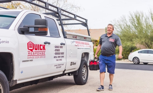 A garage door repairman walks with his toolbox away from his company truck parked on the street.
