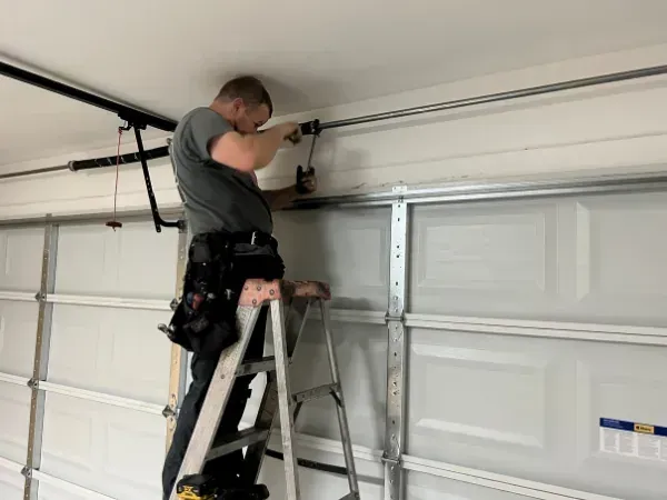 Garage door technician installing or repairing garage door hardware inside a garage.