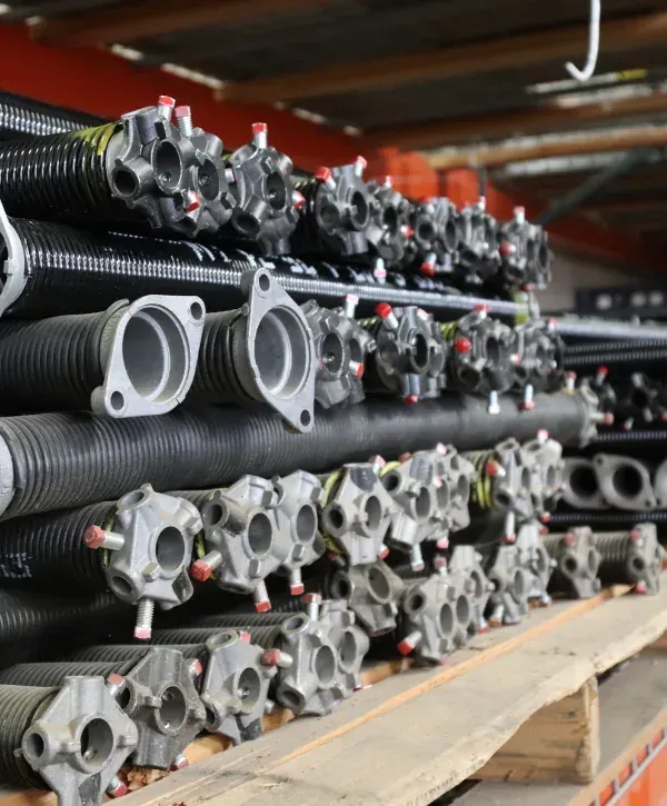 Garage door springs and replacement parts stacked on shelving in a repair shop.
