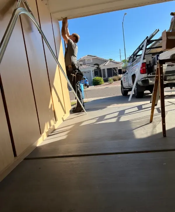 Garage door technician installing a new door panel on a suburban home exterior.