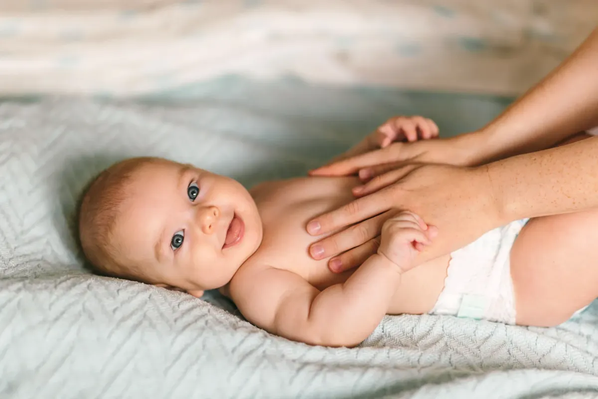 Infant's feet being held by a woman's hand with painted and manicured hands resting on a gray blanket
