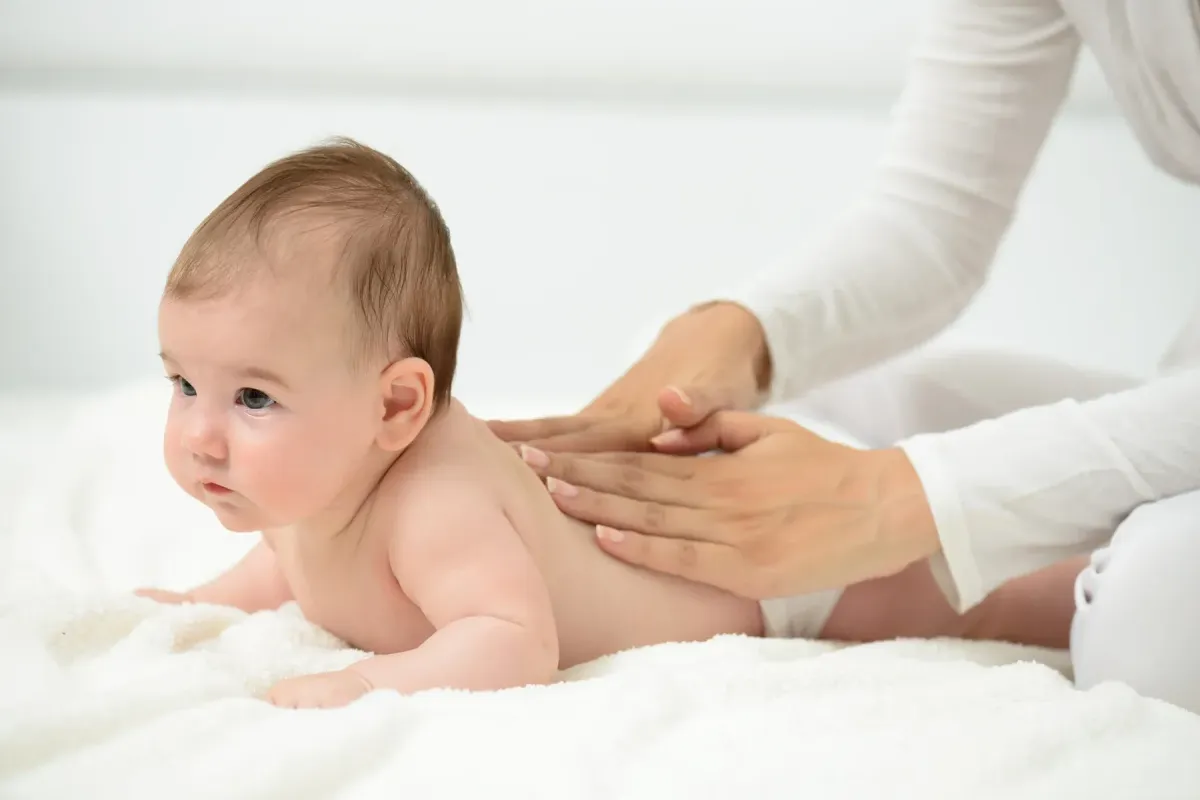 Infant's feet being held by a woman's hand with painted and manicured hands resting on a gray blanket