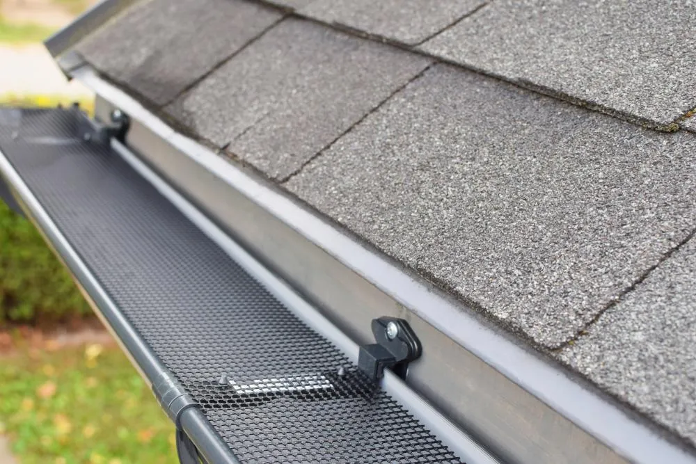Close-up of gutter guard and roof shingles showing water drainage protection system.
