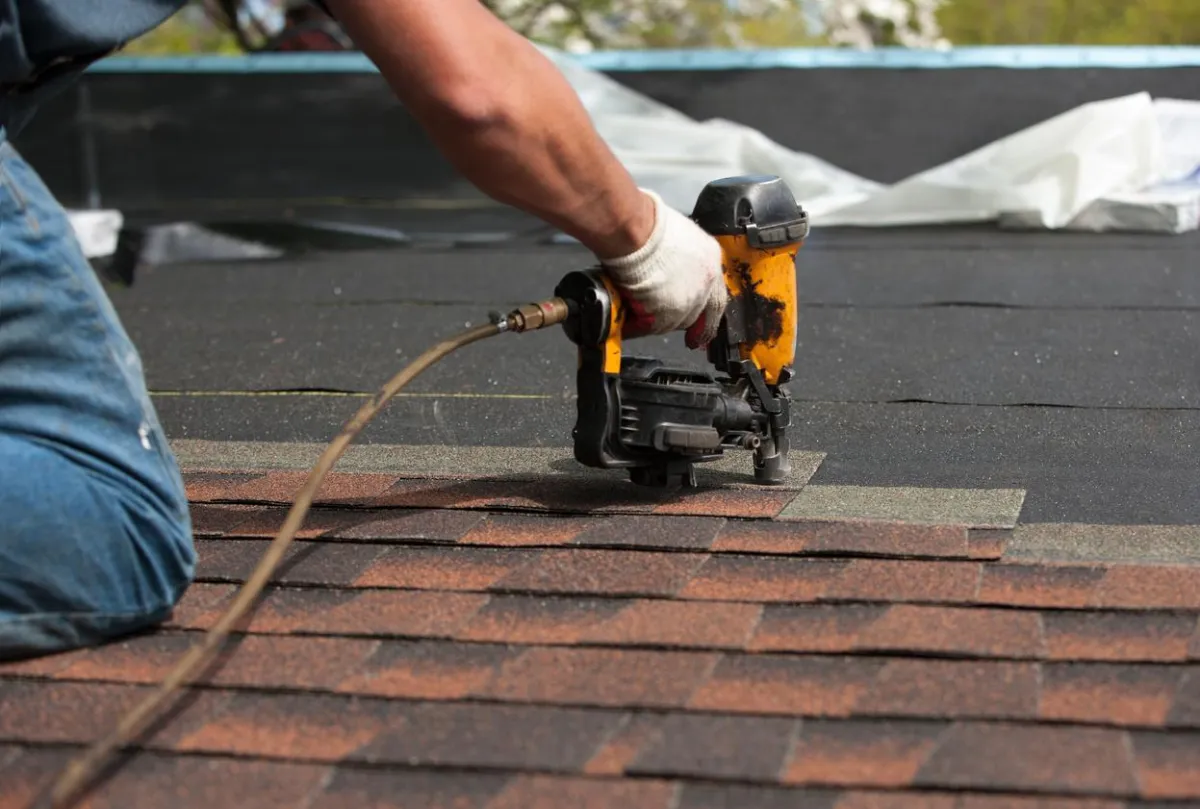 Roofing contractors installing metal panels on a sloped roof with safety equipment.