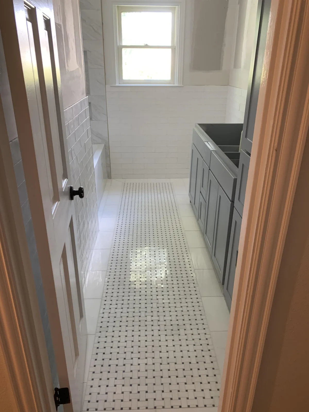 A stunning, spacious walk-in shower adorned with unique white and gray tiles on the walls, featuring two bronze shower heads and a glass divider. The floor is tiled with small white hexagons, complementing the luxurious aesthetic. Two built-in niches provide convenient storage for bath products.