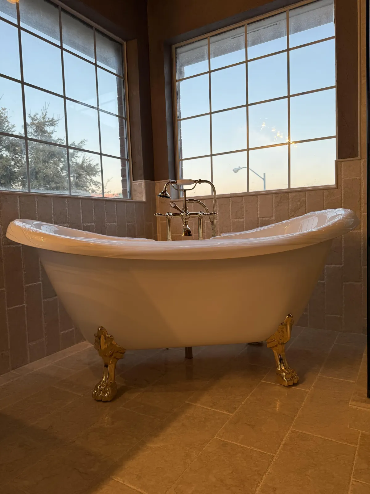 A sleek, modern shower with light gray subway tiles, a glass door, and a matching glass side panel. The shower features a small high window, brushed metal fixtures, and a floor of gray pebble tiles. 