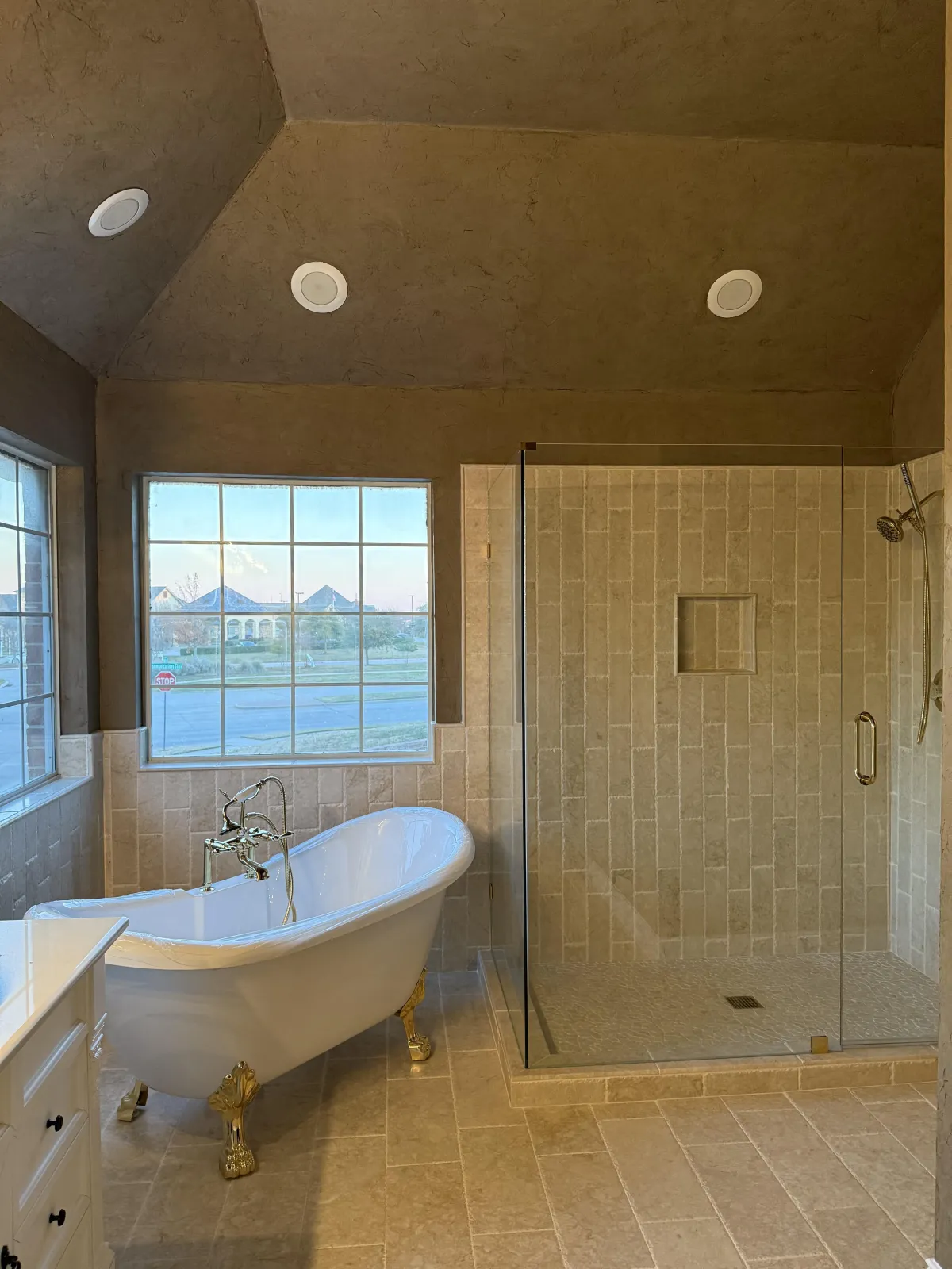 A modern bathroom featuring a large glass-enclosed shower with a bench, beige wall tiles, and a pebble tile shower floor. The room includes a wooden vanity with a white sink and a wall-mounted faucet, enhancing the clean and contemporary aesthetic.