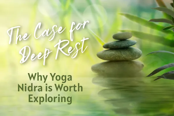 Stones piled on top of one another in a lush green pond with the caption "The Case for Deep Rest – Why Yoga Nidra Is Worth Exploring"