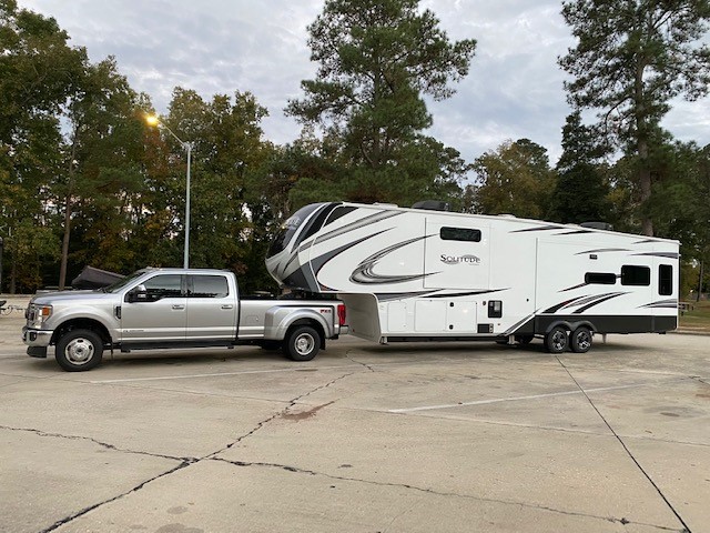 Mobile RV technician in uniform working on a large white RV in a sunlit campground, with tools neatly arranged and a sense of urgency and professionalism. The background shows a clear blue sky and green trees, emphasizing mobility and outdoor service.