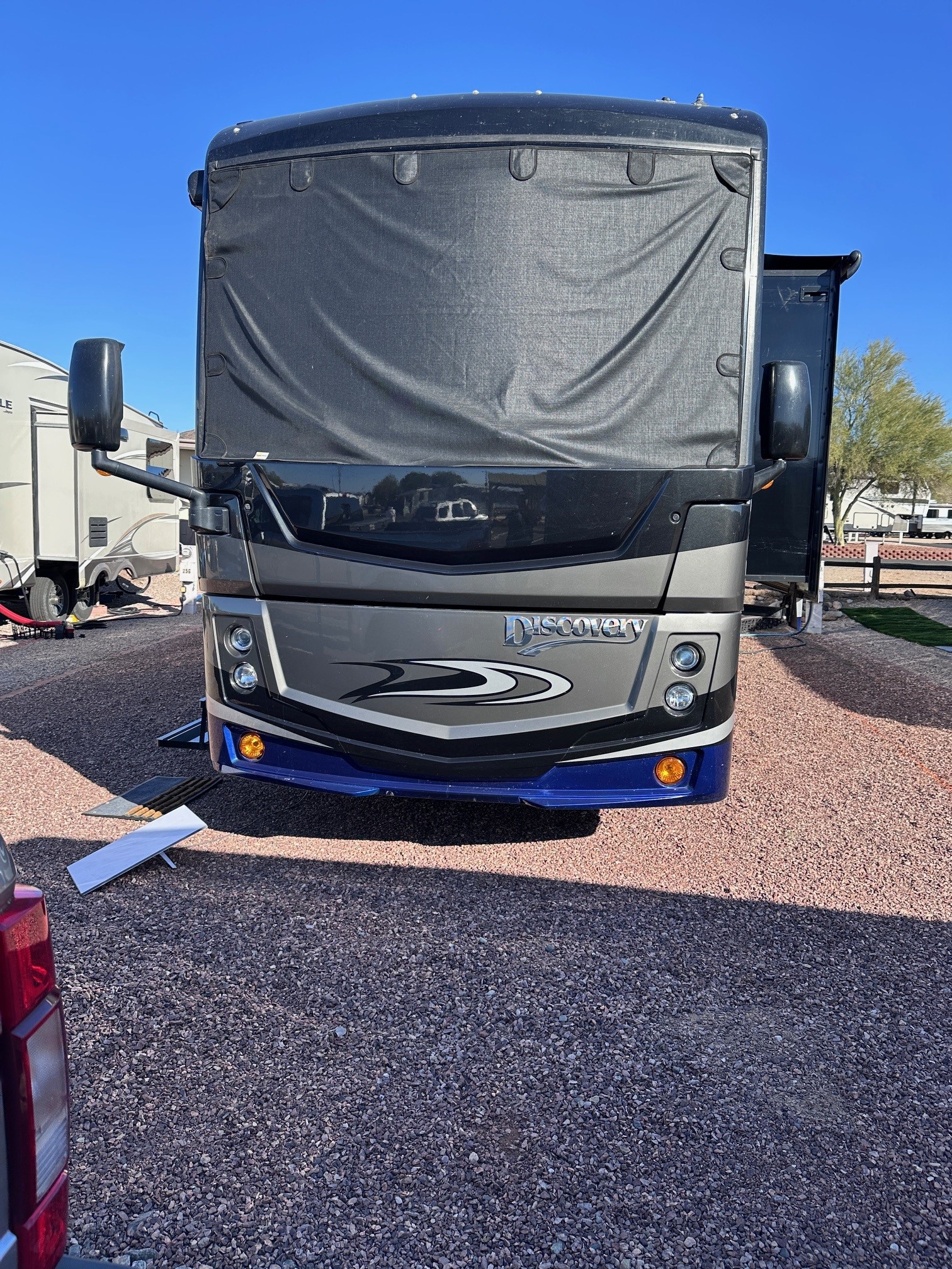 Mobile RV technician in uniform working on a large white RV in a sunlit campground, with tools neatly arranged and a sense of urgency and professionalism. The background shows a clear blue sky and green trees, emphasizing mobility and outdoor service.