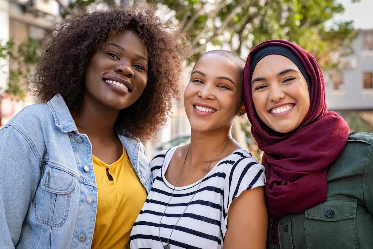 3 ladies of mixed ethnicity stay close together smiling.