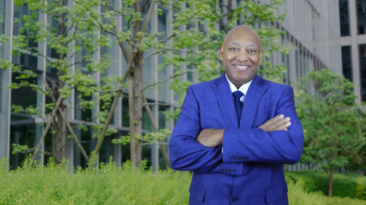 A woman in glasses stands with arms crossed outdoors.