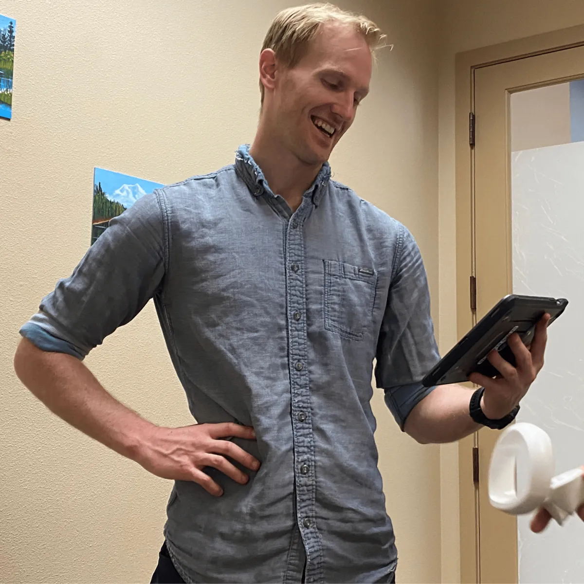 A PhysioFIT therapist smiles as he monitors a patient's progress on a tablet, ensuring a personalized and effective virtual reality therapy session.