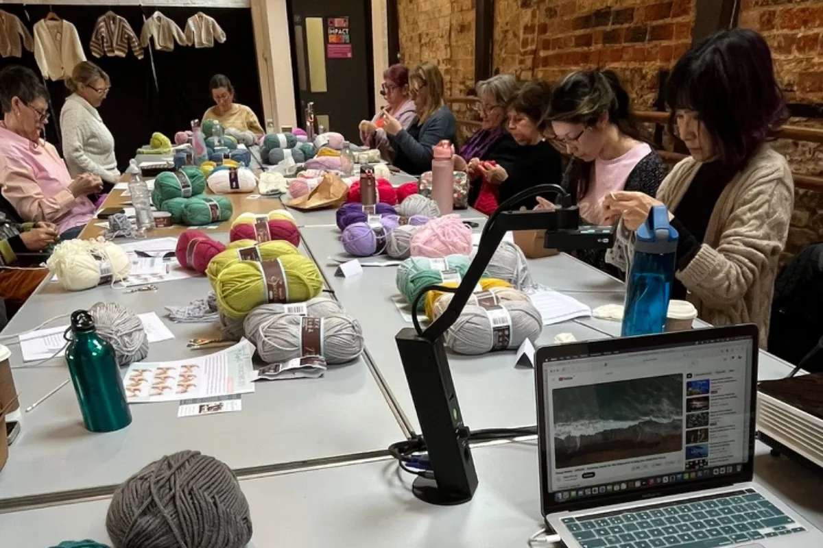 A group pf ladies gathered around  table of yarn, crocheting at a crochet workshop