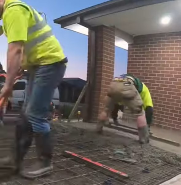 two tradies spreading concrete on rebars for a concrete slab