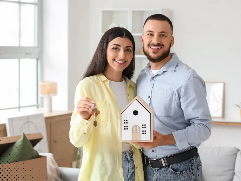 Happy homeowners holding a small house model after their home inspection, celebrating their new home in DFW, Texas